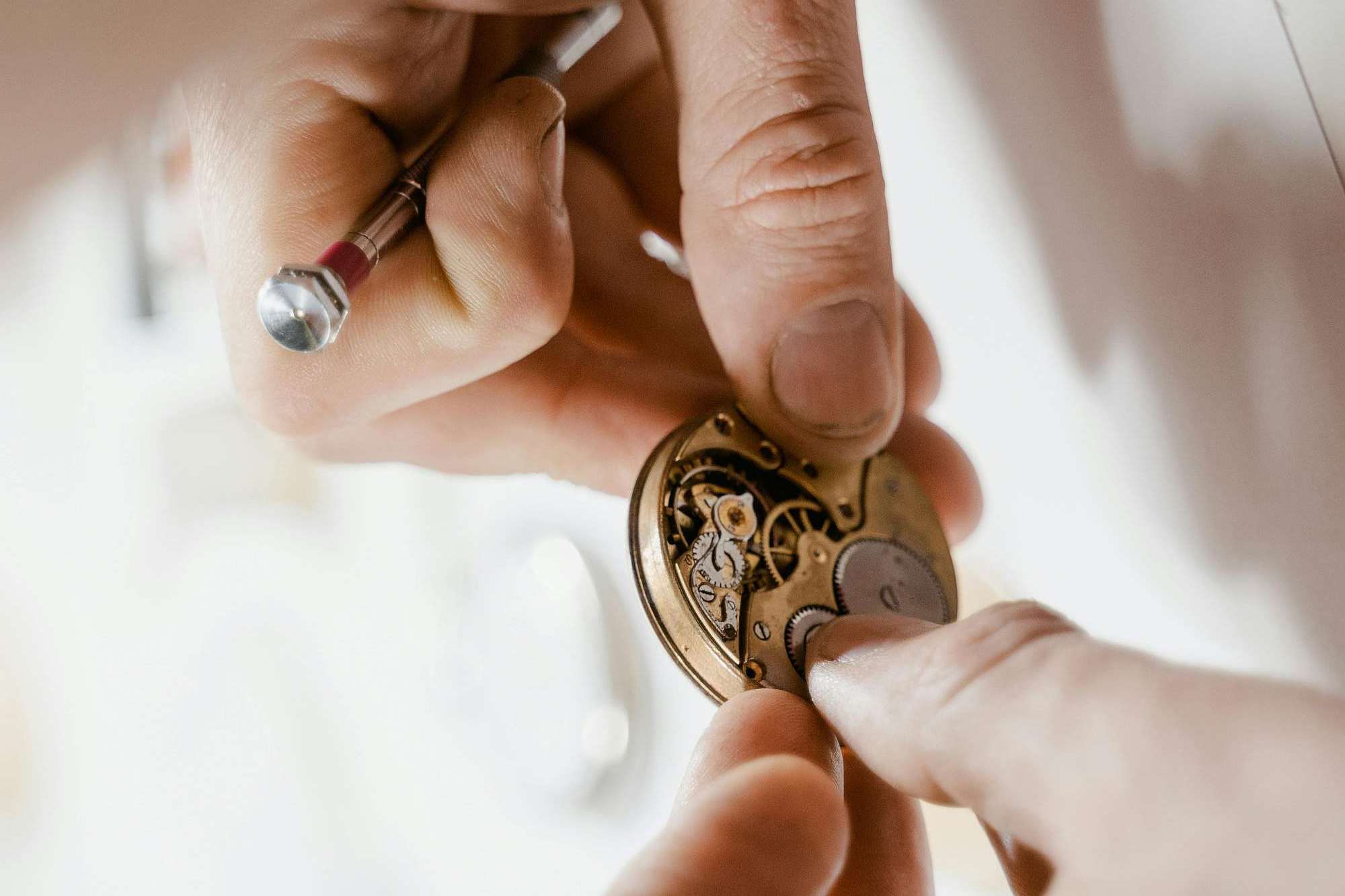 A watchmaker's hands inspecting a movement with a loupe